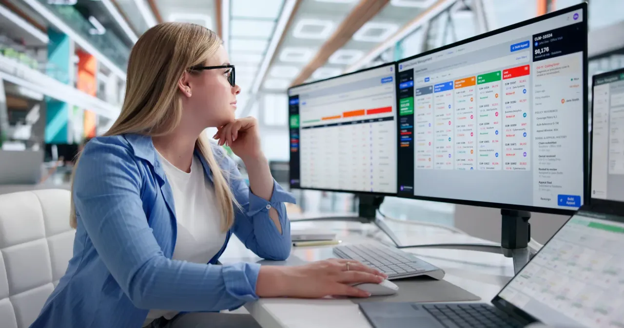 Woman reviewing dashboard data on multiple computer monitors.